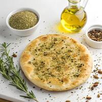 A round flatbread topped with olive oil and zaatar spice mix, golden brown and displayed on a clean white background photo