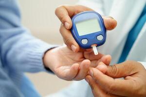 Asian doctor using digital glucose meter for check sample blood sugar level to photo