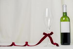 A minimalist and creative composition featuring a wine bottle, glass, red velvet ribbon on a soft cream background, representing elegance, Valentines celebration, and sophisticated design. photo
