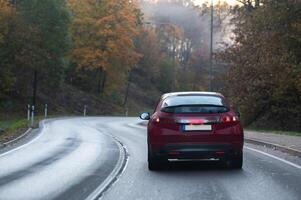 Rear view of a red car on a bend in an autumn road photo