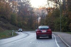 Rear view of a red car on a bend in an autumn road, speed limit sign photo
