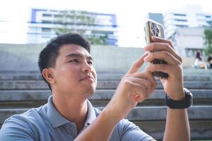 A man is looking at his phone while sitting on a set of stairs. He is using his finger to point at something on the screen photo