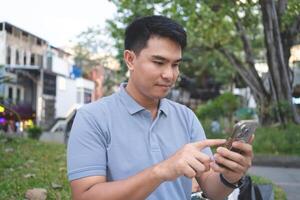 A man is looking at his cell phone while sitting on a bench. He is pointing at something on the screen photo