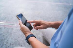 A man is sitting on the ground and using his cell phone. He is pointing at something on the screen photo