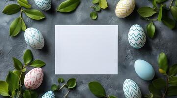 Decorated eggs and blank card surrounded by green leaves on a gray surface photo