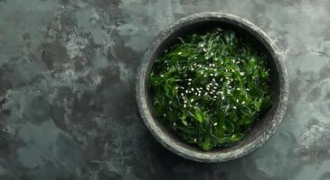Fresh seaweed salad in stone bowl with sesame seeds on a dark surface photo