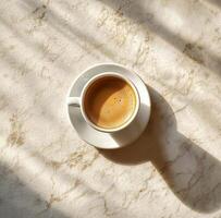 Warm cup of coffee sits on a marble table with sunlight casting shadows in the morning photo