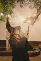 Man dressed in wizard attire performing magic in a whimsical garden at twilight photo