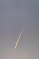 Airplane contrail streaking across a clear blue sky during twilight hours photo