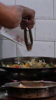 chefe de cozinha mexer fritar legumes dentro uma flamejante wok dentro a ao ar livre cozinha. pessoa cozinhando Comida usando uma flambar técnica, acendendo quente óleo e álcool dentro uma frigideira. fechar acima super lento movimento cenas video