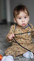 Lovely boy sitting on the carpet at home holding a shoe lace. Black domestic cat jumping near the kid and stops looking at child. Vertical video