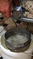 Man opens the faucet at honey extracting machine. Fresh golden organic liquid honey flows into the bucket standing under the equipment. Vertical video