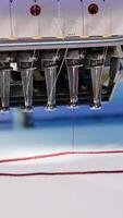 Automatic embroidery machine is working. Sewing machine needle in motion. Sewing machine needles with different colors moves up and down on white fabric. Close-up. Vertical video