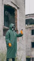 Human in protective suit and gas mask in abandoned place. Survivor holding a mobile phone while standing in ruined city. Post-apocalyptic world after a nuclear war. Vertical video