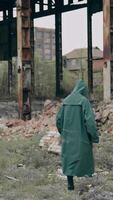 Person in chemical protective suit walking in distracted place. Survivor in abandoned place with piles of garbage from ruined buildings. Apocalypse concept. Vertical video