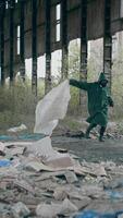 Survivor running in abandoned place. Human in protective suit and gas mask with cloth runs madly in ruined building on garbage background. Vertical video