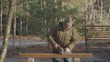 An experienced man uses a power tool to process a metal beam while standing in a serene forest. The sun shines through the trees, enhancing the tranquil atmosphere. video