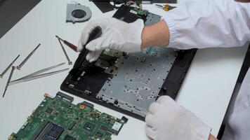 A technician is carefully working on a laptop's internal components in a tidy workspace. Various tools are organized around them for effective repairs. video