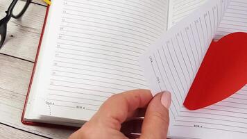 A person holding a red heart shaped paper in front of a notebook video