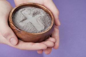 Hands with gray ash cross on purple background. Ash Wednesday photo