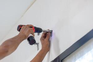 Male technician hands using a electric screwdriver install curtain rods, Man installing furniture and equipment in the living room photo