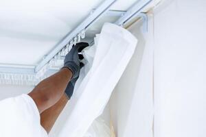 Worker man hand hanging window curtain, Repairman installs a curtain rod and hangs curtains in the house photo