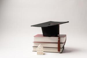 Graduation Cap Resting on Stacked Books With a Small House Figurine Beside It in a Minimalistic Setup photo