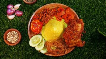 Top View A serving of cone-shaped yellow rice paired with crispy chicken, fried vermicelli, sambal, cucumber slices, sambal egg, and spices like red onions and peppercorns. photo