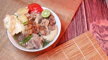 Sop buntut or oxtail soup in a white bowl with fresh potatoes, tomatoes, lime and fried onions. Served in a traditional style on a bamboo mat and burlap. Space for text available photo
