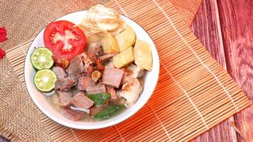 Delicious clear beef soup garnished with fresh potatoes, tomatoes, lime and fried onions. Served in a traditional style on a bamboo coaster. Space for text available photo