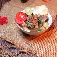 Beef ribs soup or sop Iga with beef bone, potato, fresh tomato, lime slices, and fried shallot. Served on bamboo mats, burlap, and leaves. Space for text available photo