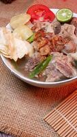 Closeup oxtail soup or sop buntut with potatoes, tomatoes, lime slices, and fried shallots. Served on a bowl white with Bamboo mat and burlap. Space for text available photo