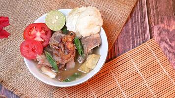 Closeup of a bowl of Beef ribs soup or sop Iga with beef bone, potato, fresh tomato, lime slices, and fried shallot. Served on bamboo mats, burlap, and leaves. Space for text available photo