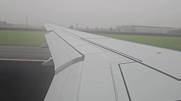 Airplane taking off in heavy fog. A view from inside an airplane, showing its wing as the aircraft moves along a runway at an overcast airport. video