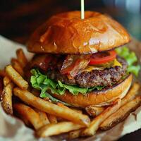 beef burger with crispy bacon and vegetables and fries on small black plate and glass of beer on wooden background photo