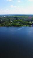 Smooth calm surface of the blue river with sparkles from the sun. Beautiful green city locating near the river. Top view. Vertical video