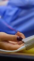 Female hand with bright manicure and sensor during surgical operation. Close up. Blurred background. Vertical video