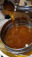 Fresh honey leaking from the faucet of honey extracting machine after pumping. Liquid organic product flowing on the sieve. Top view. Vertical video