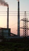 Panoramic view on harmful power station at sunset. Tall electricity pylons next to large factory with smoke stacks on the evening sky. Camera rising up. Vertical video