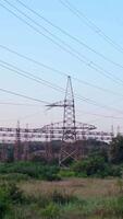 Lots of electricity towers on field. Large power station with many high-voltage electric lines with wires against the sky background. Transmission lines in green nature. Vertical video