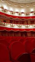 panorâmico Visão do lindo ricamente decorado teatro corredor. linhas do vermelho cadeiras dentro teatro corredor. grande esvaziar teatro com não pessoas. vertical video