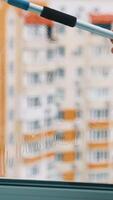 Wiping window with a brush. View from flat on a plastic window cleaning with a special tool in the city. Housekeeping concept. Vertical video