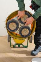 Individual in green jacket and black pants inspects a floor polishing machine with three circular pads on a light wooden floor near a white wall. photo