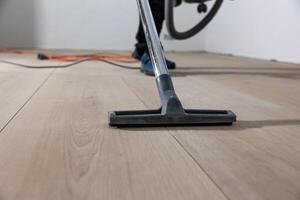 Light colored wooden floor with visible grain patterns being polished. An orange power cord and a person in blue shoe covers are partially visible. photo