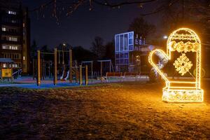 A playground at night features a glowing mitten shaped light with snowflake designs, climbing structures, swings, benches, and a residential building. photo