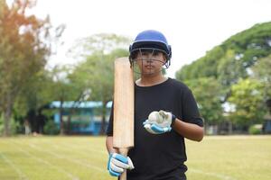 Cricket player wearing cricket Helmet holds a bat and ball in his hand, standing on the grass while practicing. photo