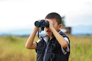 thai boy uses binoculars to explore nature in the field. the concept of learning outside the classroom nature study, exploration. photo