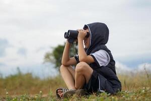 a boy uses binoculars to explore nature in the field. the concept of learning outside the classroom nature study, exploration. photo