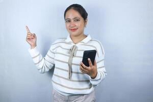 Beautiful smiling Asian woman in sweater pointing side with finger while holding phone photo