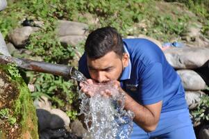 Man drinking water from a garden fountain with selective focus, highlighting the refreshing moment and lush surroundings photo